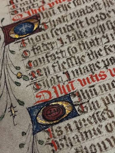 A close-up of an illuminated medieval manuscript page with gold-leaf initials